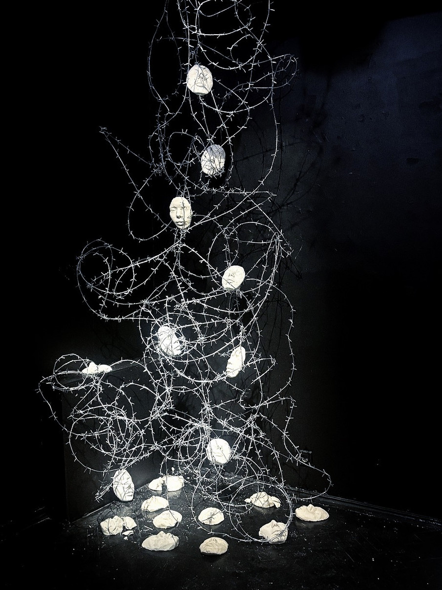 Horizon, 2025: the full installation in a darkened room — barbed wire falling from ceiling to floor, holding plaster casts of the artist's face, with more casts lying on the ground. Installation view, Khodyinka Gallery.